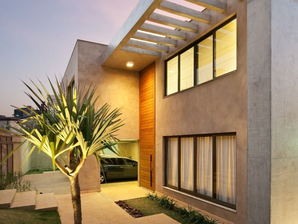 Fachada com pergolado de concreto e porta de madeira na construção de casa no bairro Santa Lúcia, Belo Horizonte, pela Mazí Construtora.