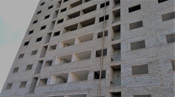 Obra em alvenaria estrutural de blocos de concreto em execução; fiadas niveladas, juntas alternadas, cintas e graute visíveis — canteiro limpo.