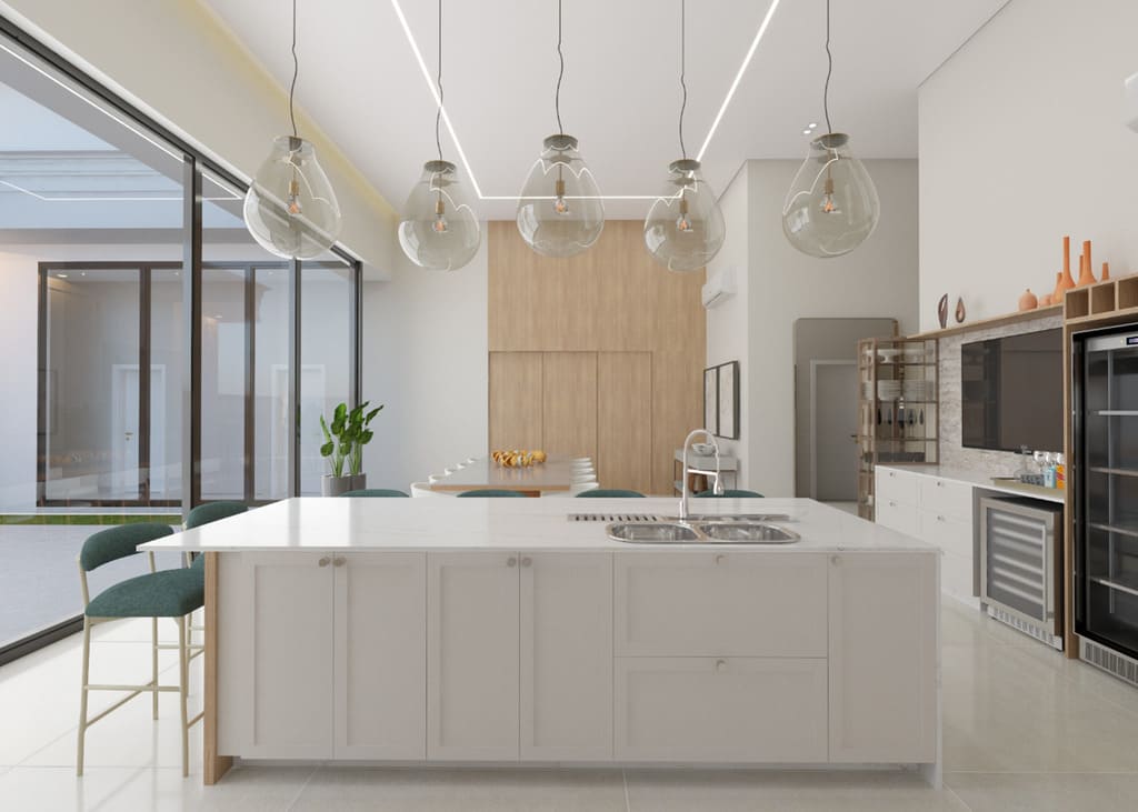 Cozinha planejada com ilha branca, cinco pendentes de vidro alinhados, trilhas de LED lineares no teto e grande esquadria lateral trazendo luz natural — sem pessoas.
