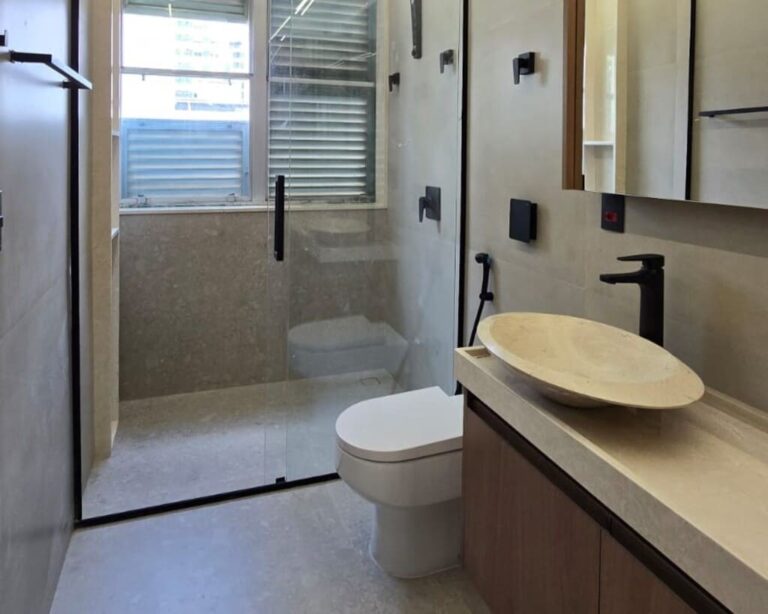 Banheiro de apartamento reformado com cuba esculpida em pedra natural e metais pretos.