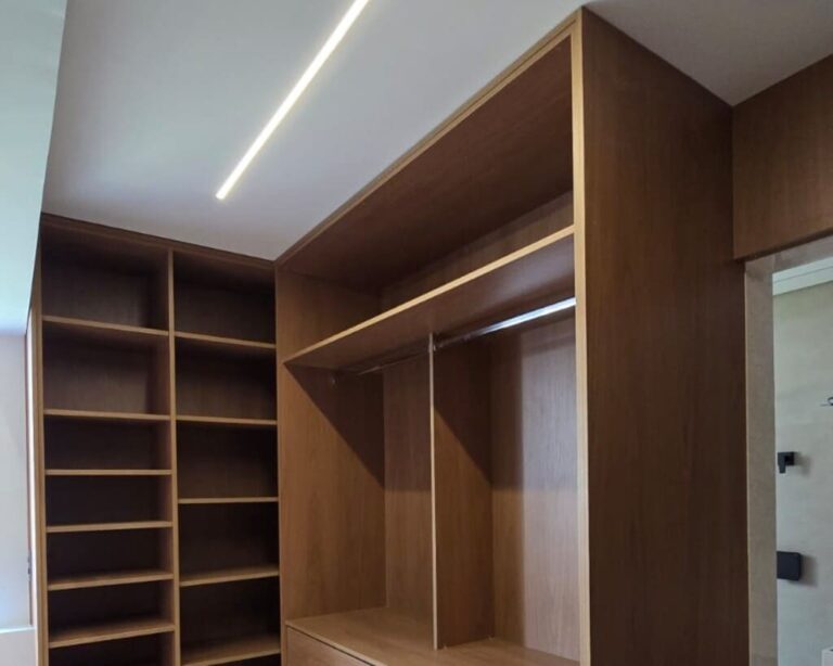 Suíte com painel amadeirado, cabeceira estofada e iluminação embutida.