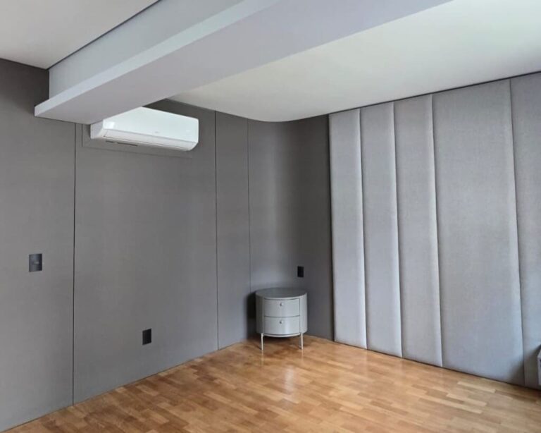 Suíte em tons de cinza com piso em taco, cabeceira estofada e mesa de cabeceira lateral.